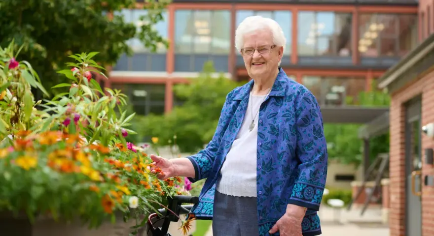 An elderly woman smiles, tending to flowers outside the St. Rose of Viterbo Convent.
