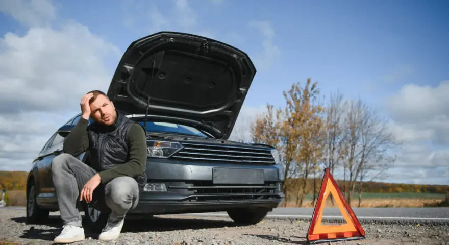 Zrezygnowany mężczyzna przy zepsutym aucie z otwartą maską i trójkątem ostrzegawczym. Może to być początek jego rozważań, jak zezłomować auto.