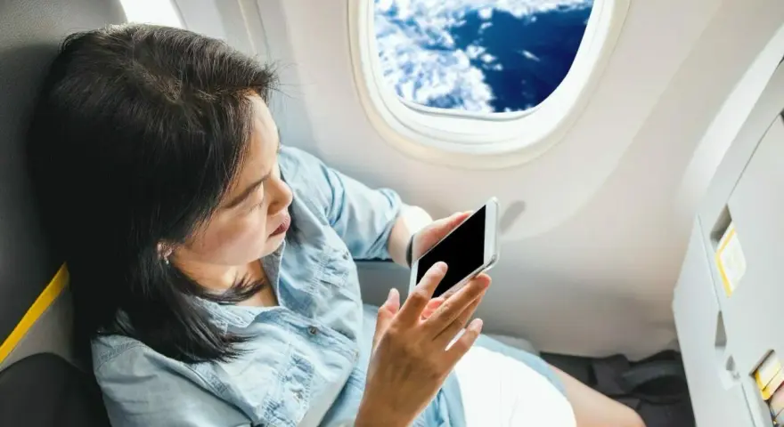 Kobieta z telefonem siedzi przy oknie w samolocie Ryanair, podziwiając chmury.