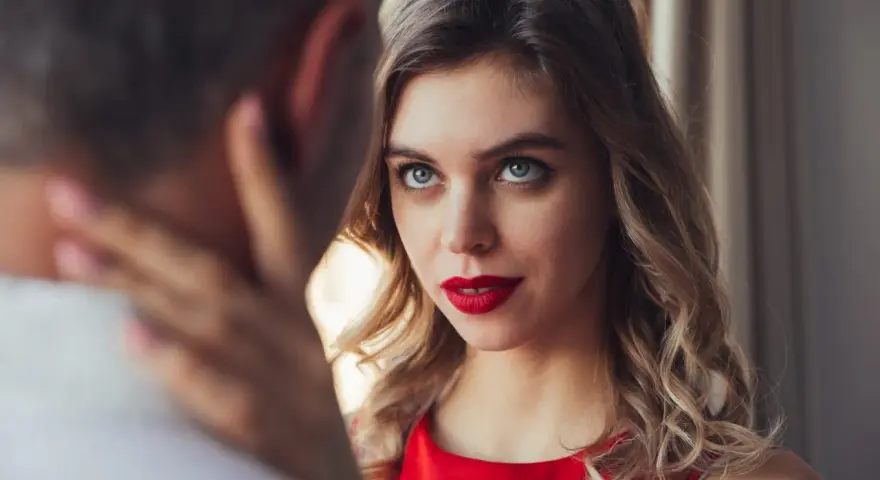 Un homme regarde intensément une femme aux yeux bleus et aux lèvres rouges, vêtue d'une robe rouge.