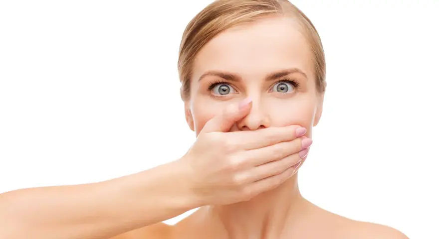 Zaskoczona kobieta zakrywa usta dłonią, jakby poczuła nagły metaliczny posmak w ustach.