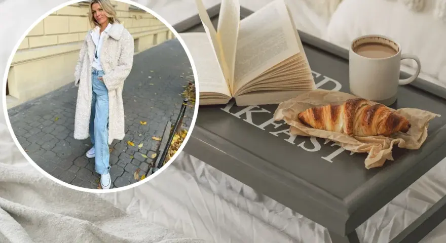 Kobieta w płaszczu z owczej wełny, symbolizującym quiet luxury, cieszy się śniadaniem w łóżku: książka, croissant i kawa.