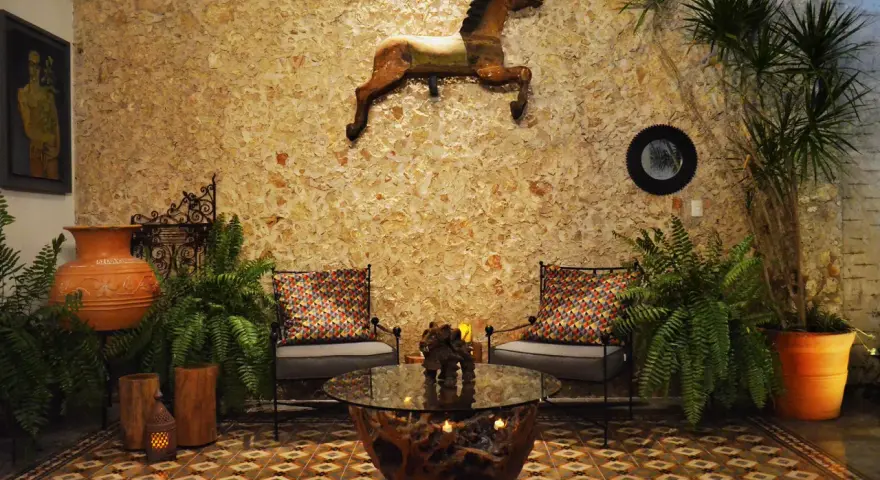 Un caballo decorativo adorna la pared de un patio exterior, complementado por plantas exuberantes y un rincón acogedor.