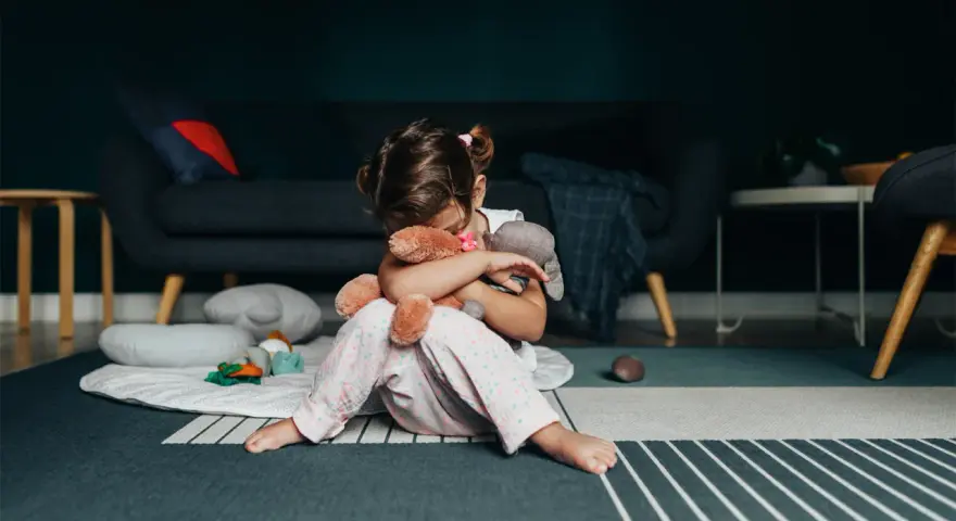 Smutna dziewczynka tuli misie, zastanawiając się nad przyczynami padaczki u dzieci.