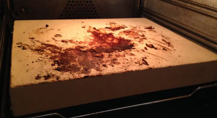 Ein schmutziger pizzastein mit braunen Flecken und Essensresten, der im Ofen liegt.
