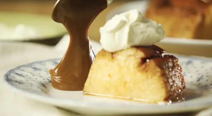 Un trozo de flan de 12 huevos, cubierto con caramelo y crema batida, servido en un plato con diseño azul.