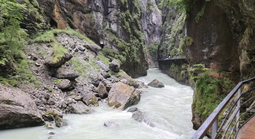 Aare Gorge, with its powerful river and dramatic cliffs, leads towards the Reichenbach Falls. A wooden walkway hugs the canyon wall.