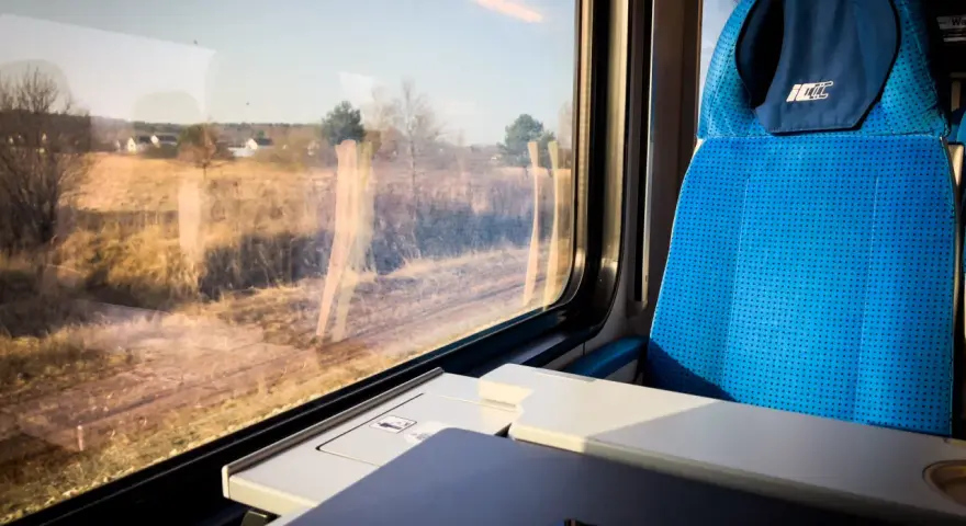 Podróż pociągiem z Katowic do Krakowa Balic. Widok z okna na krajobraz, obok niebieskie siedzenie i stolik z laptopem.