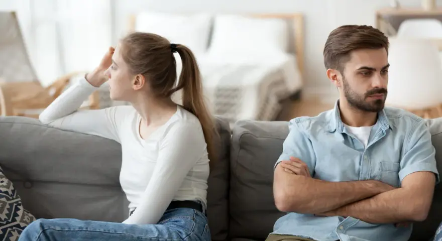 Couple marié, domicile différent, impôt. Ils sont assis sur un canapé, dos à dos, visiblement en désaccord.