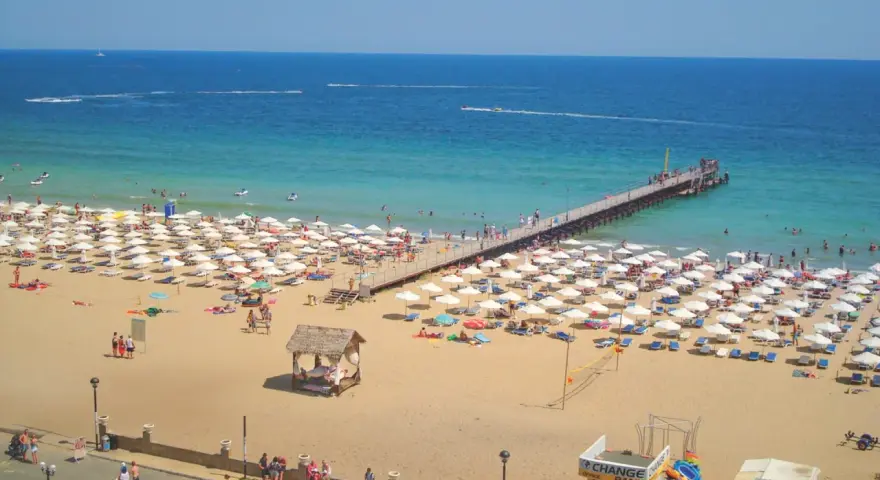 Słoneczny Brzeg, Bułgaria: tłumy plażowiczów, białe parasole, molo i turkusowe morze.