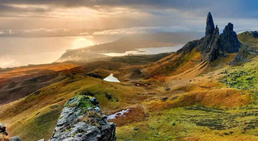 Paysage écossais spectaculaire, photo HDR. Des collines ondulantes aux teintes dorées et vertes, des lacs scintillants et des formations rocheuses imposantes sous un ciel dramatique.