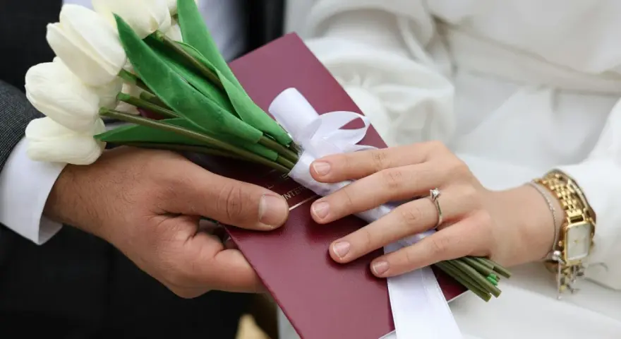 Para weselna trzyma bukiet białych tulipanów i akt małżeństwa. Zastanawiasz się, ile się daje na wesele?