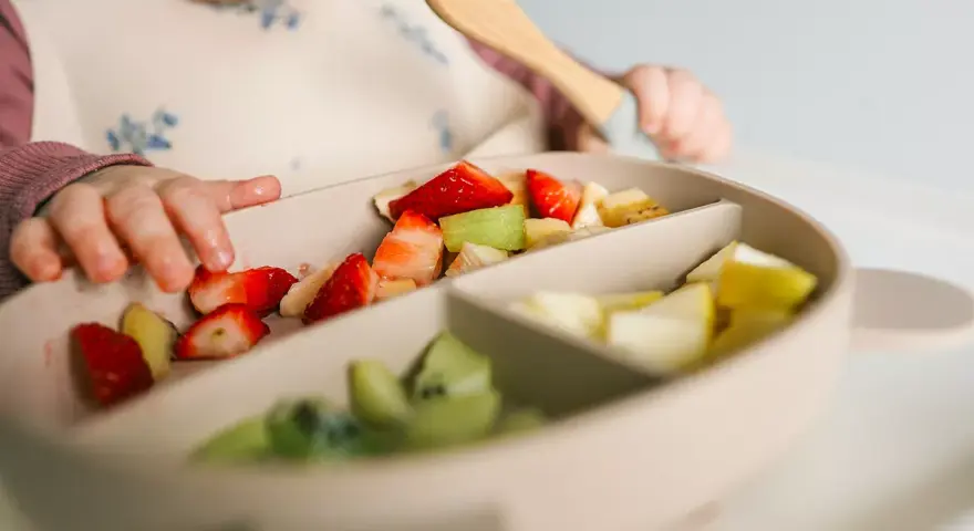 Bebé explorando fresas, kiwi y plátano en su plato. Es un buen momento para ofrecer fruta a los bebés.