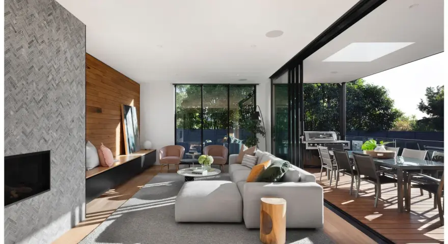 Elegante salón con chimenea de piedra, pared de madera y grandes ventanales que conectan con una terraza. Un ejemplo de las últimas tendencias interiorismo.