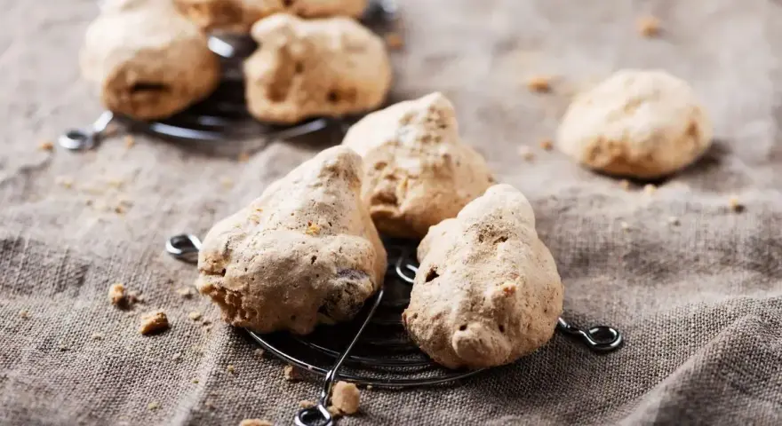 Biscotti meringati, dall'aspetto rustico, brutti ma buoni, su una griglia metallica e un telo grezzo.