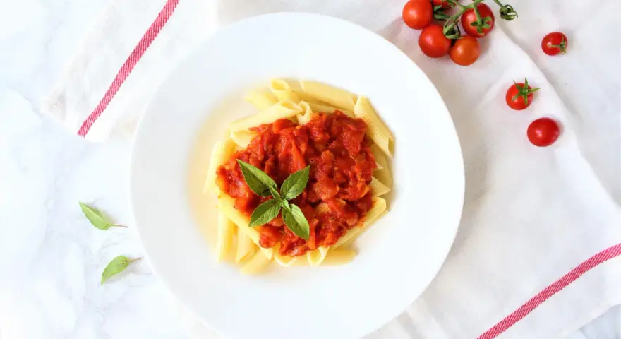 Penne z sosem pomidorowym i bazylią, obok świeże pomidorki koktajlowe.
