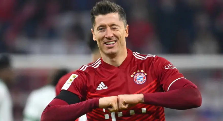 Piłkarz Robert Lewandowski w czerwonej koszulce Bayernu Monachium, uśmiecha się i zaciska pięści.