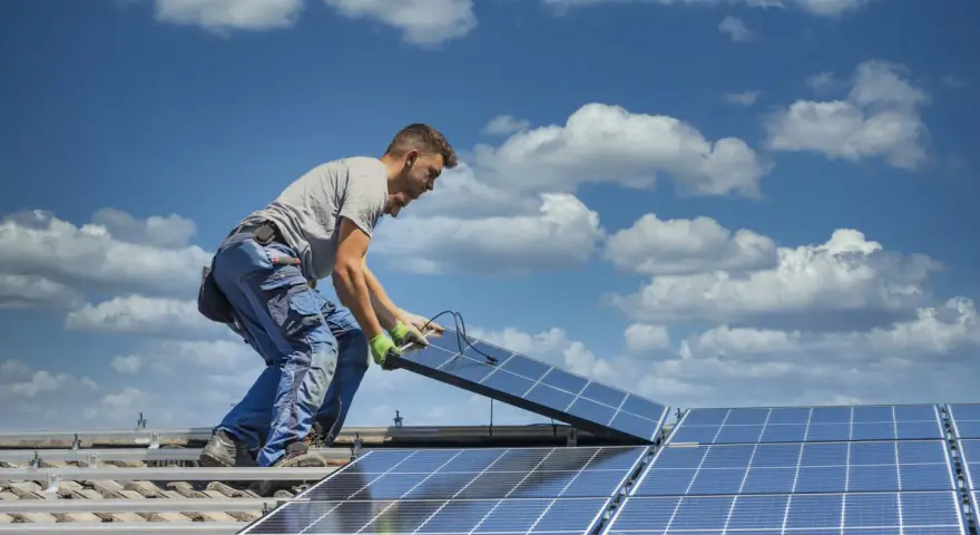 Instalator montuje panele fotowoltaiczne na dachu. Optymalne ustawienie paneli wschód-zachód zapewnia maksymalne wykorzystanie energii słonecznej.