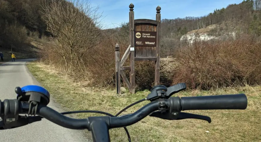 Rowerem przez Ojcowski Park Narodowy. Wita nas drewniany drogowskaz i malownicze wapienne skały w tle.