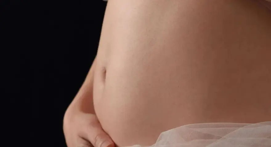 Pancia gonfia e dura, sembro incinta. La pelle liscia e chiara, con un leggero velo di tessuto rosa chiaro.