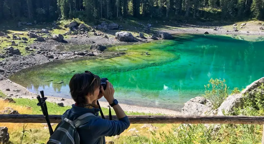 Donna con zaino e macchina fotografica cattura la bellezza del lago di Carezza, in Trentino Alto Adige.