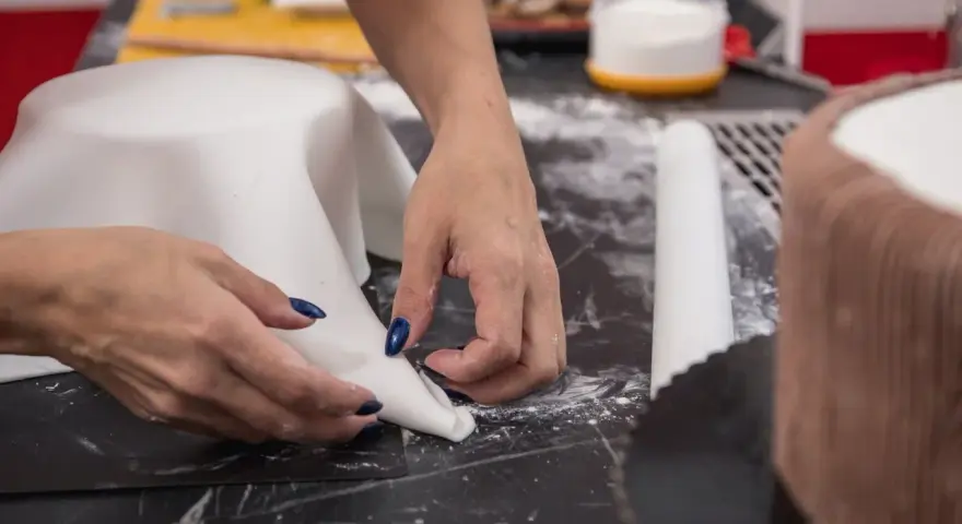 Hände formen weißen Fondant für eine Torte. Hier sind Tipps zum Fondant ausrollen für perfekte Ergebnisse.
