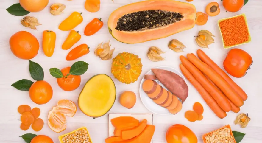 Różnorodne pomarańczowe owoce i warzywa: papaja, marchew, bataty, pomarańcze, morele, kaki, dynia, papryczki.
