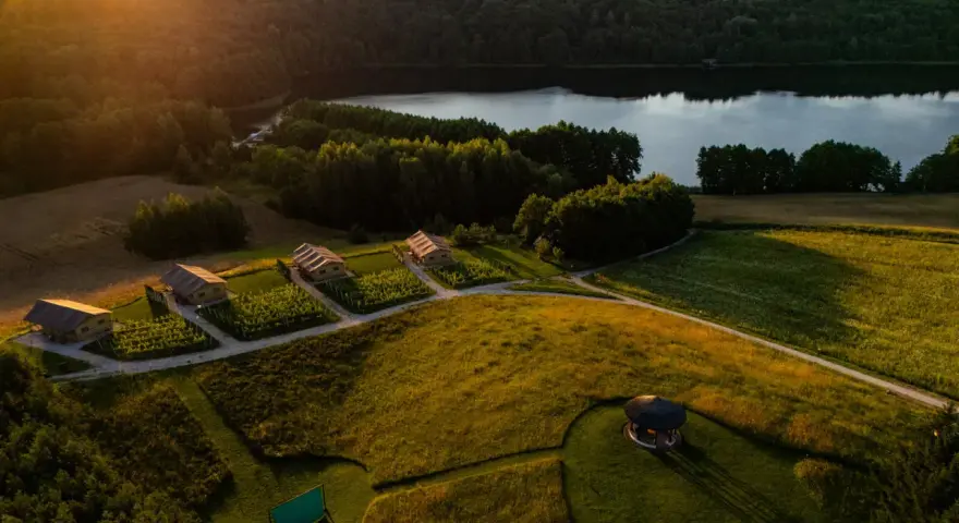 Malownicze domki nad jeziorem, idealne na fajne miejsca na wakacje. Słońce zachodzi, rzucając złote światło na pola i lasy.