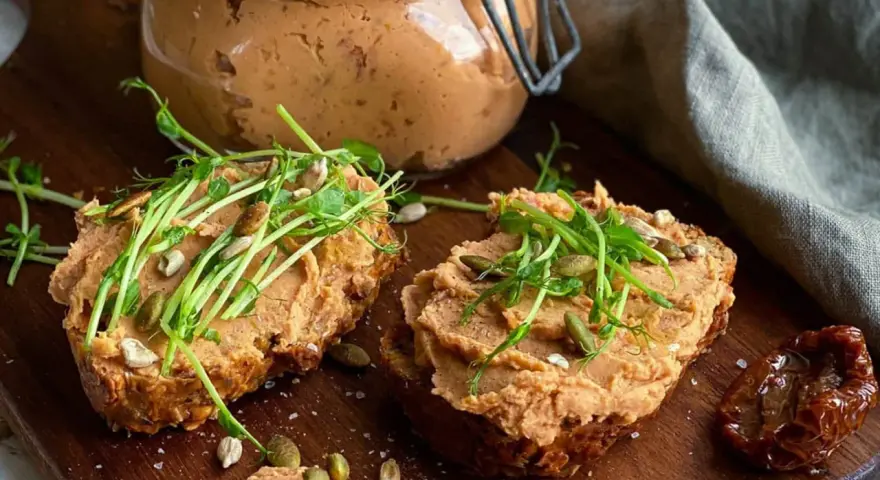 Två rostade brödskivor med krämigt refried beans, toppade med groddar och frön. En burk med pålägget syns i bakgrunden.