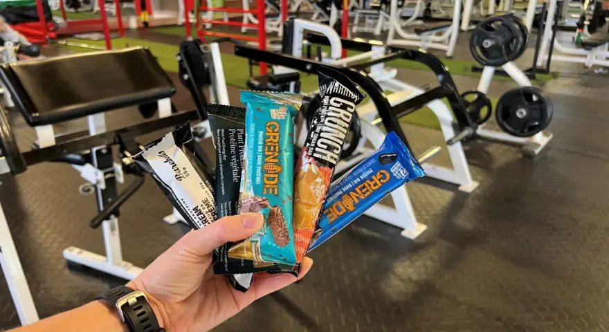Une main tient plusieurs barres protéinées, parfaites comme collation avant ou après le sport, dans une salle de sport.