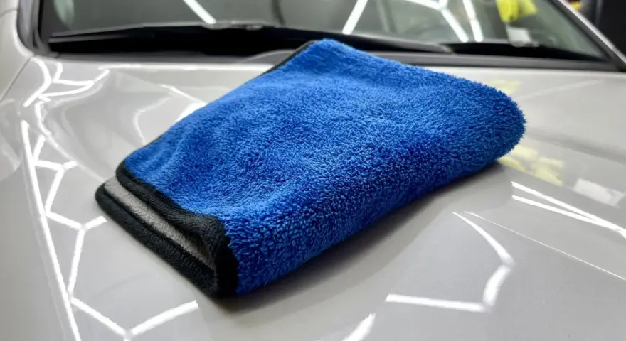 En blå torkhandduk ligger på en skinande vit bilhuv. Perfekt för att torka av bilen efter tvätt.