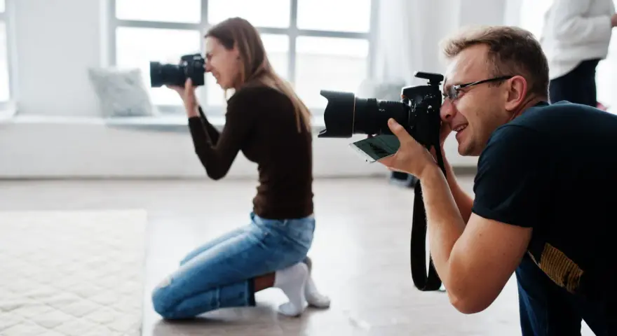 Dwóch fotografów klęczy i robi zdjęcia aparatem w jasnym studiu.