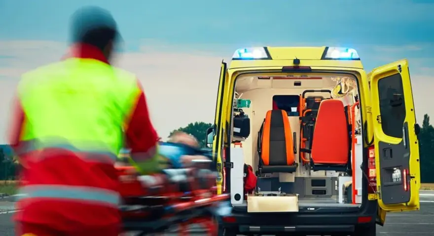 Ratownictwo medyczne w akcji. Ratownik w kamizelce odblaskowej transportuje pacjenta do karetki.