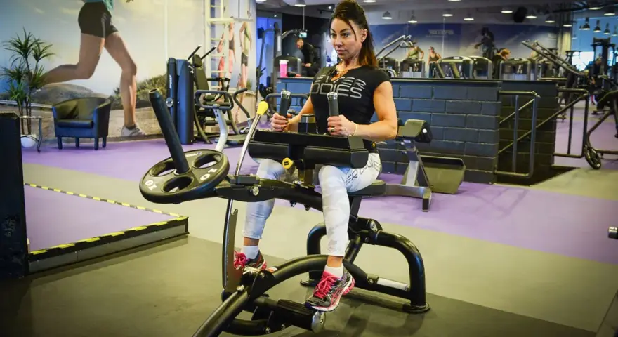 Kvinna tränar på gymmaskin. Hon har på sig träningskläder och fokuserar på sin träning. Hon verkar vara en seriös atlet som tar sin vad press på allvar.