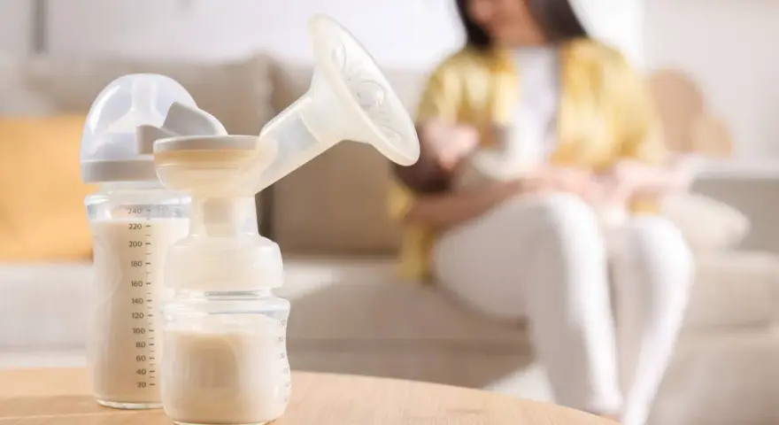 Biberon e tiralatte con latte materno, mentre una mamma allatta il suo bambino. Scopri come aumentare il latte materno in modo naturale.