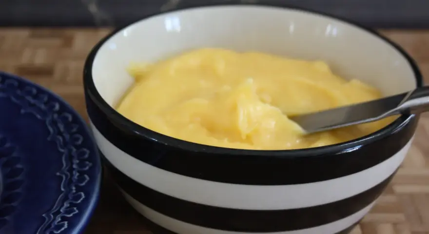 En skål med krämig, gul lemon curd, redo att bredas på en blå tallrik.
