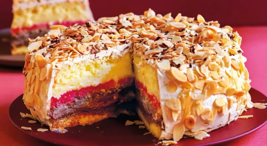 Una fetta di pizza dolce abruzzese, stratificata con crema, cioccolato e confettura, ricoperta di mandorle tostate e scaglie di cioccolato.