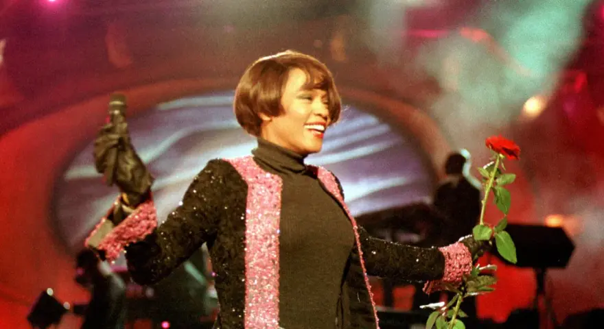 Whitney Houston z mikrofonem i czerwoną różą podczas niezapomnianego koncertu w Polsce.