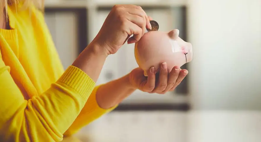 Persona con suéter amarillo deposita moneda en hucha. Un asesor fiscal te ayuda a ahorrar.