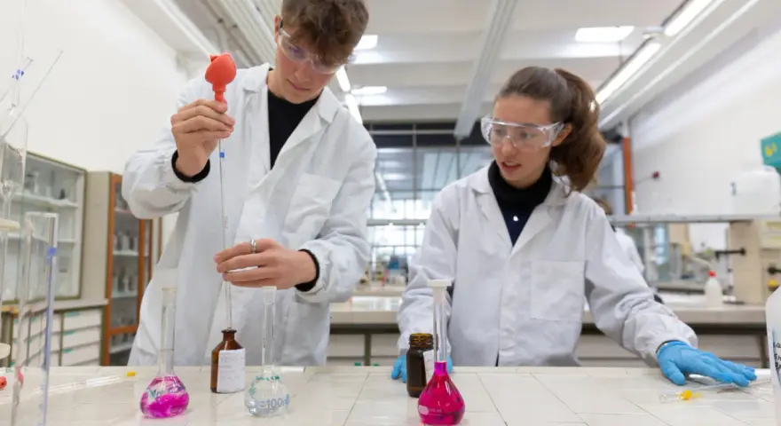 Ragazzi in camice bianco e occhiali protettivi eseguono esperimenti in laboratorio, un passo verso il loro futuro diploma perito chimico.