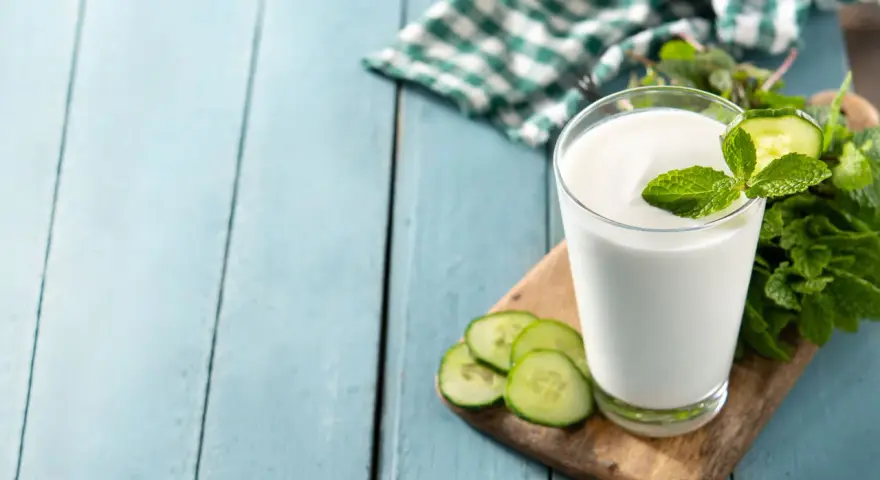 Szklanka białego napoju, idealna na kefir w ciąży, ozdobiona plasterkami ogórka i miętą.