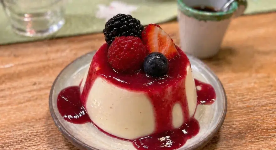 Cremige Panna Cotta mit Beeren und rotem Fruchtsirup auf einem Teller.