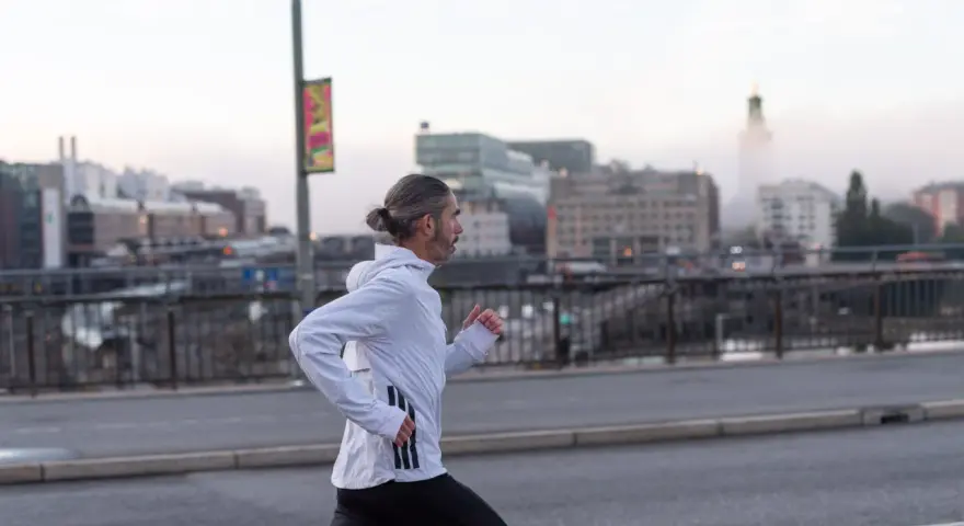Man med hästsvans springer på en bro i Stockholm, klädd i adidas halvmarathon-kläder.