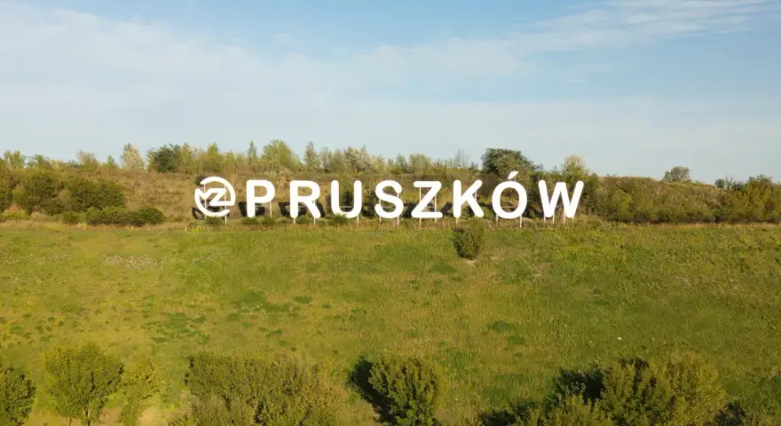 Napis "Pruszków" na tle zielonego wzgórza. Zastanawiasz się nad cenami mieszkań Pruszków?