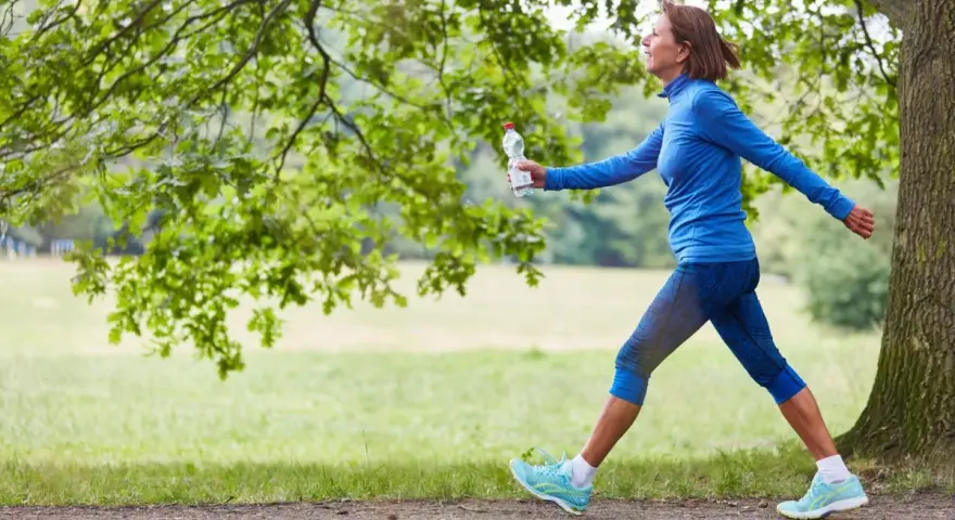 Femme souriante en tenue de sport bleue, profitant de 30 minutes de marche rapide par jour dans un parc verdoyant.