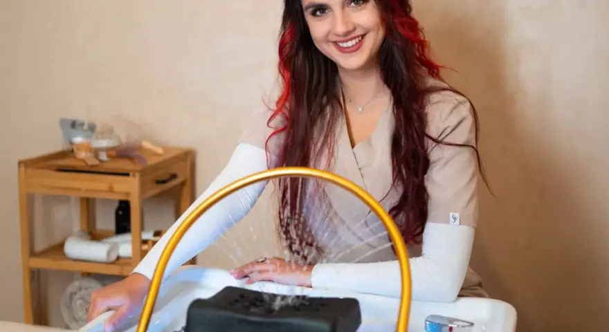 Uśmiechnięta stylistka z rudymi pasemkami przygotowuje się do zabiegu. Dowiedz się, ile kosztuje pedicure w tym salonie.