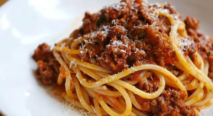Pyszne spaghetti bolognese z bogatym sosem mięsnym i startym parmezanem na białym talerzu.