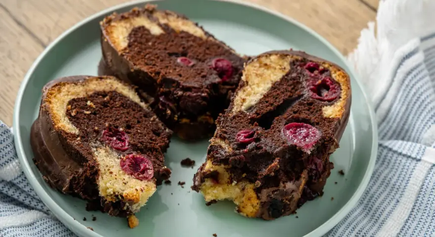 Saftiger Marmorkuchen mit Kirschen, überzogen mit Schokolade, auf einem Teller angerichtet.