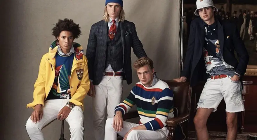 Quatre jeunes hommes posent dans un style preppy, arborant des vestes colorées, des pulls rayés et des pantalons blancs.