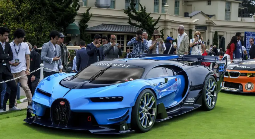 Niebieski Bugatti Veyron z numerem 16 na masce, otoczony tłumem ludzi robiących zdjęcia, na tle eleganckiego budynku.